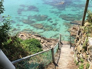 A staircase leading down to a rocky shoreline with clear turquoise water. - Casa Aurita (Sanxenxo)