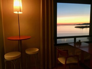A room with a view of a sunset over water, a table, two stools, and a chair. - Casa Aurita (Sanxenxo)