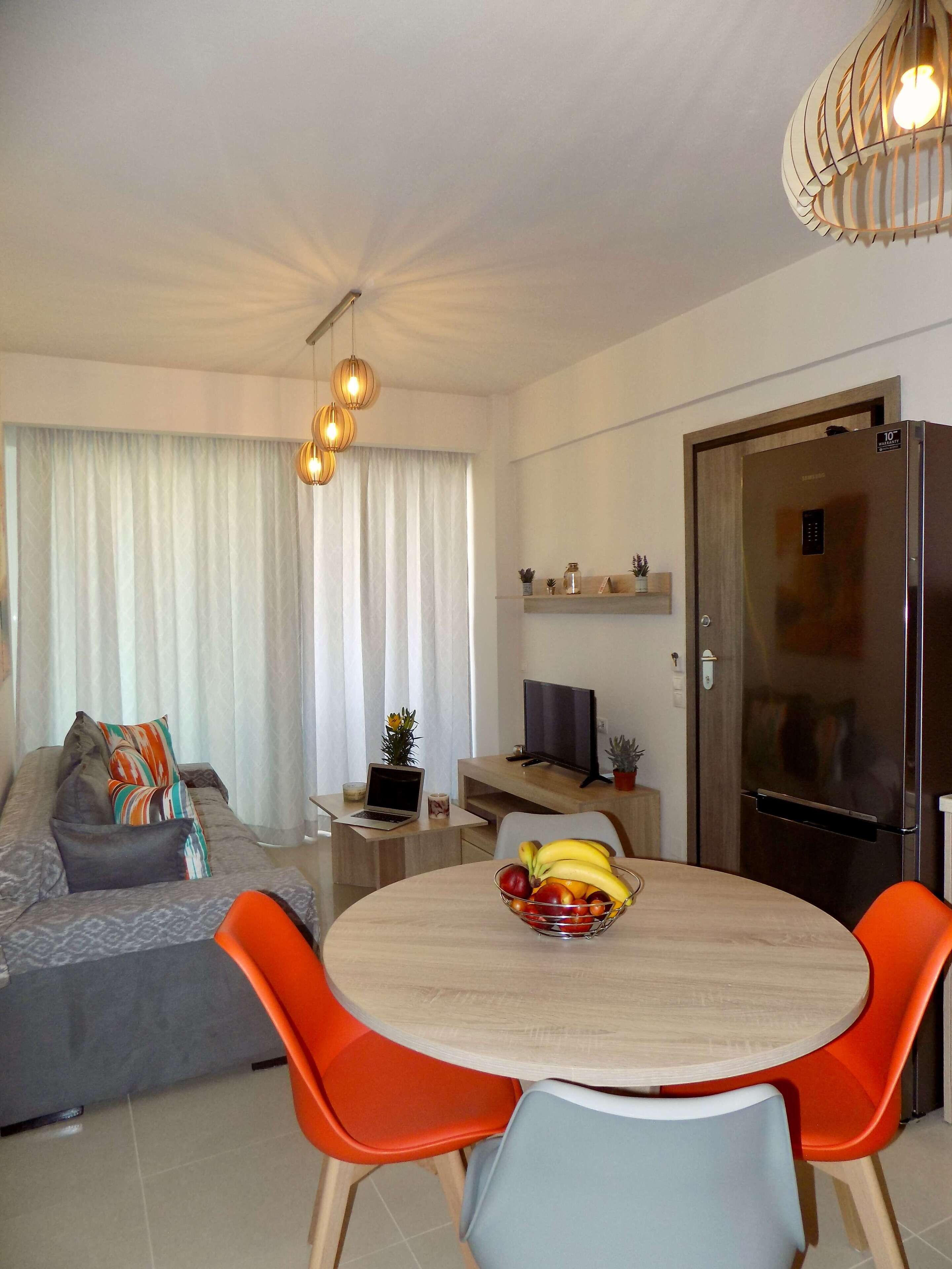 A modern living room with a sofa, a dining table with fruit, and a TV.