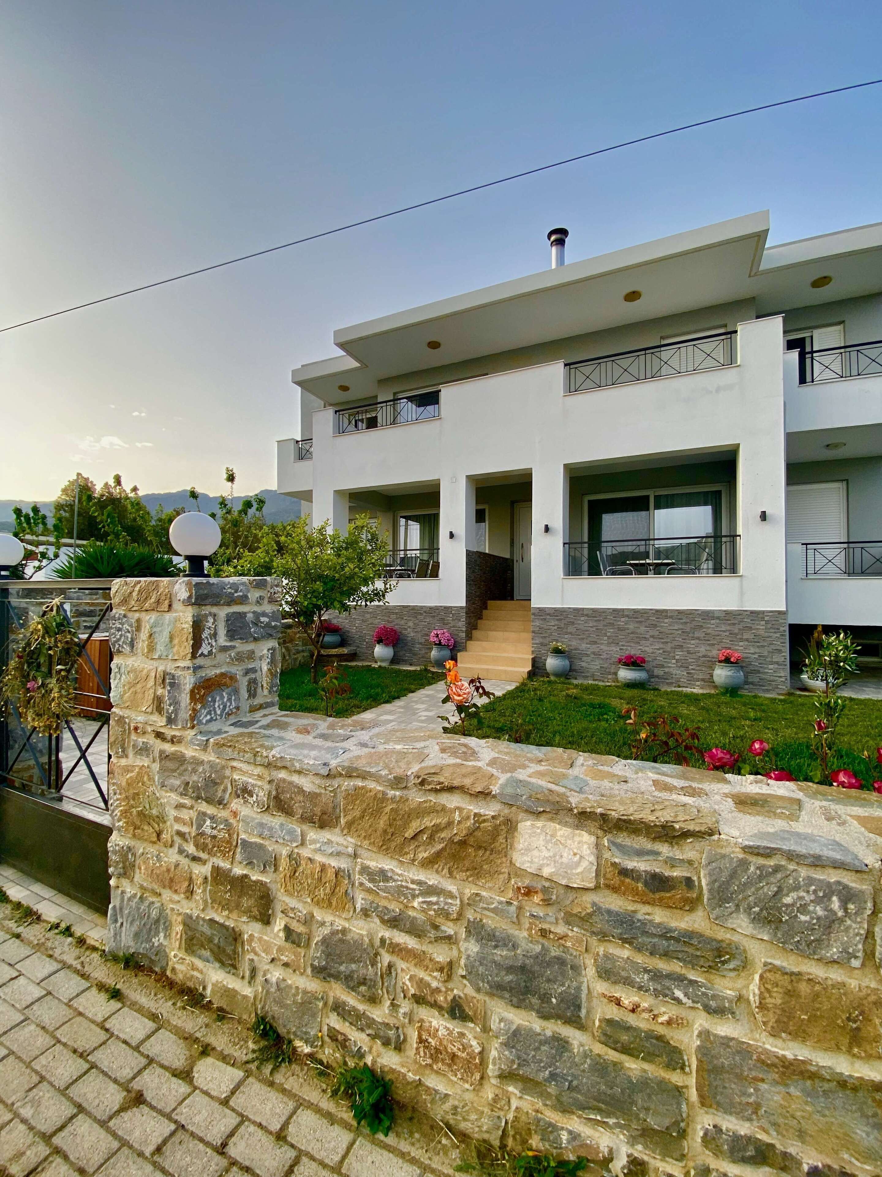 A modern two-story building with a stone facade, a balcony, and a small garden with potted plants.