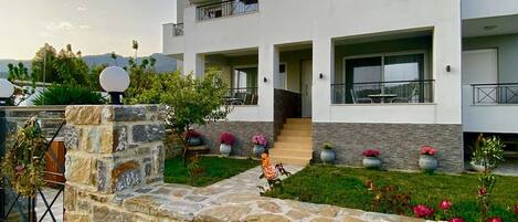 A modern two-story building with a stone facade, a balcony, and a small garden with potted plants.