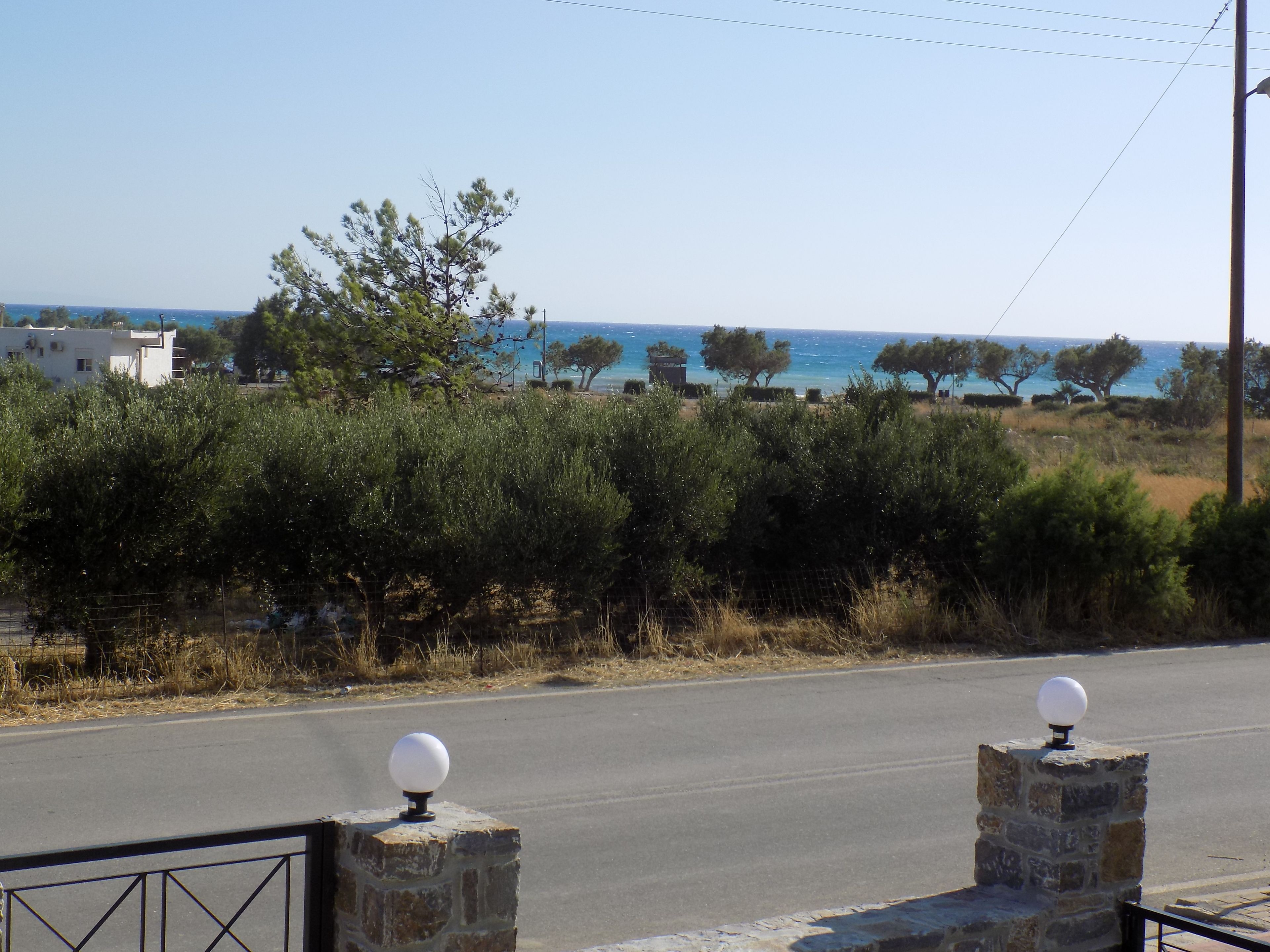 Eine Küstenstraße mit Steinsäulen, wolkenlosem Himmel und Blick auf Meer und Bäume.
