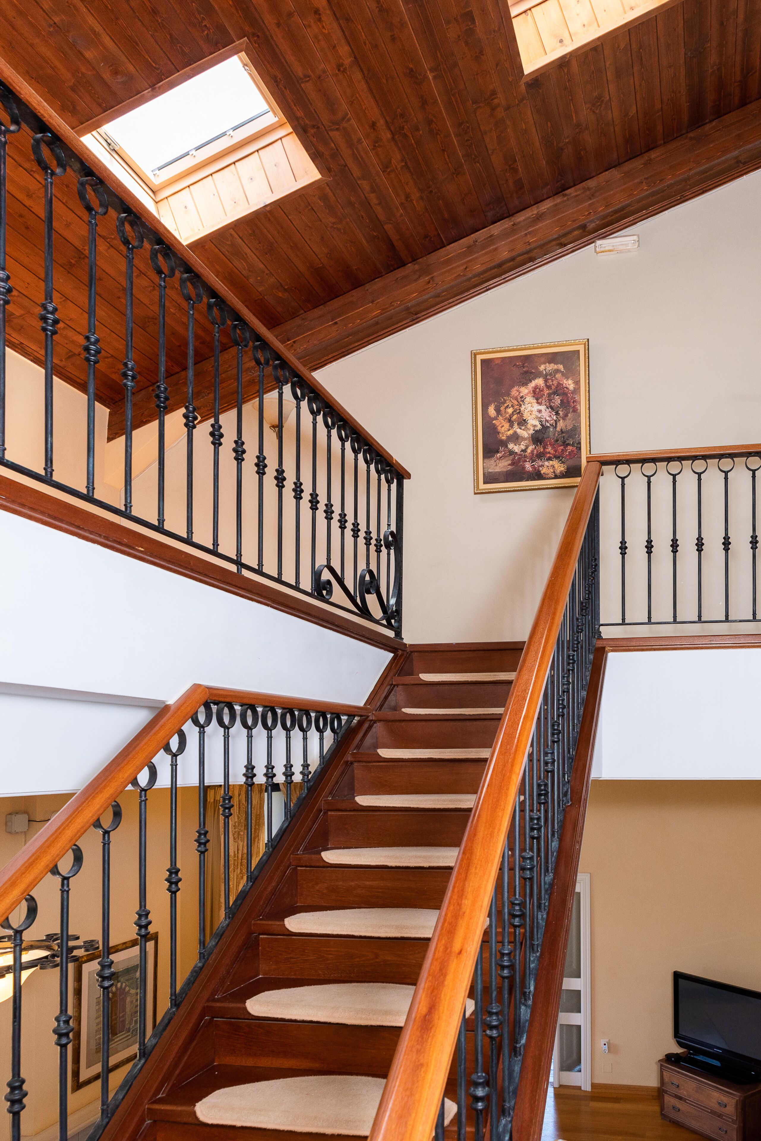 A wooden staircase with black balusters and a skylight above.