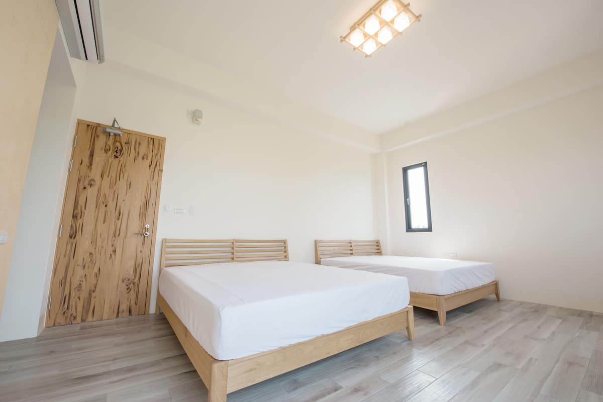 Una habitación con dos camas, piso de madera, una puerta de madera y una lámpara en el techo.
