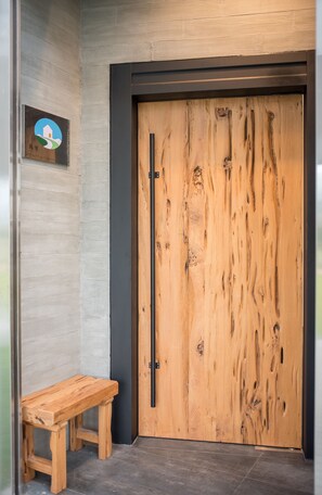 A wooden door with a black handle, a wooden bench, and a wall-mounted sign with a logo. - Here is BNB (Zhongpu)