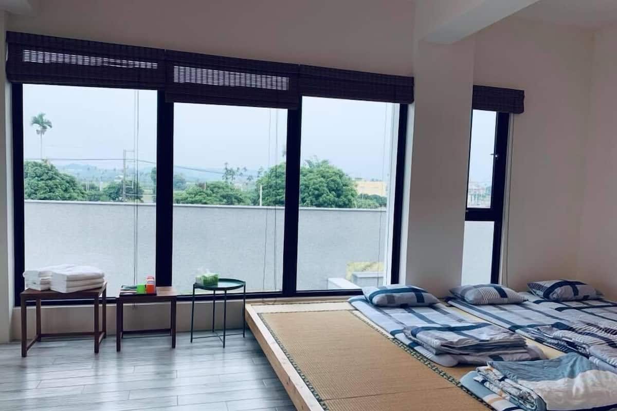 Habitación de hotel con una cama grande, una mesita con una silla y vistas a un paisaje urbano a través de amplios ventanales.