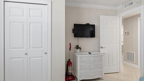 A room with white double doors, a white dresser, a mounted television, and a red vacuum cleaner.
