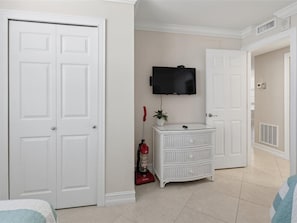 A room with white double doors, a white dresser, a mounted television, and a red vacuum cleaner.