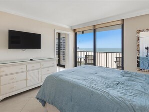 A bedroom with a bed, a television, a sliding glass door leading to a balcony with a view of the beach. - Beachfront 2BR/2BA condo in Marco Island with pool, WiFi, and kitchen. (Marco Island)