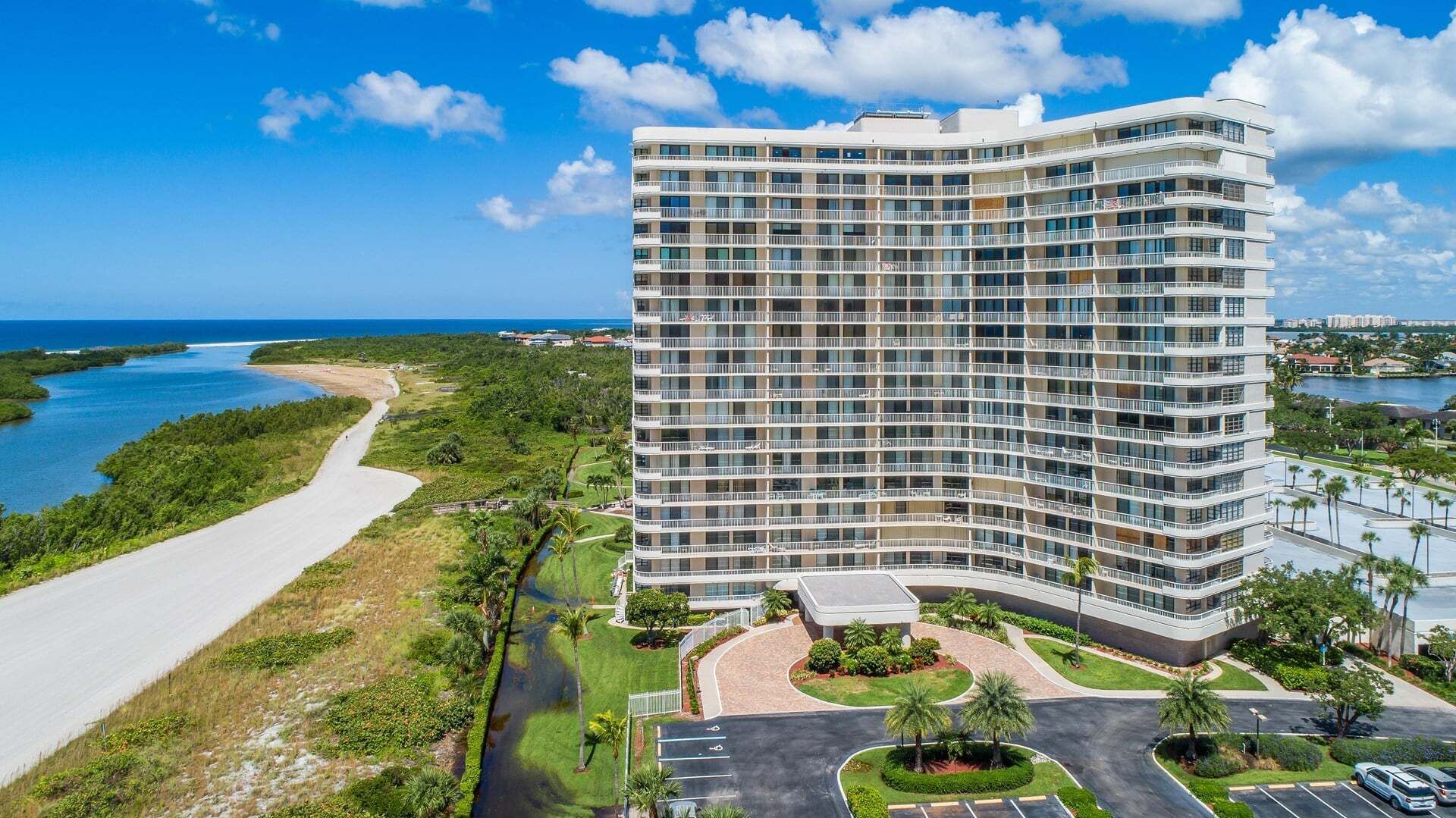 A multi-story hotel with a curved facade, located near a beach and water body.
