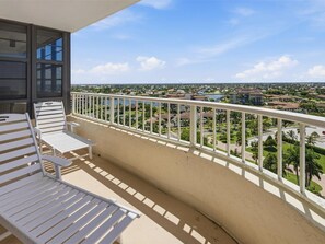A balcony with a view of a residential area, a railing, and two white lounge chairs. - Beachfront 2BR/2BA condo in Marco Island with pool, WiFi, and kitchen. (Marco Island)