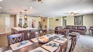 A spacious living area with a dining table set for six, a leather sofa, and a kitchen in the background. - Lake Havasu Home w/ Pool, Near London Bridge! (Lake Havasu City)