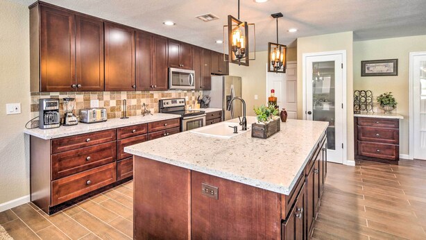 A spacious kitchen with dark wooden cabinets, a large island with a sink, and modern appliances. - Lake Havasu Home w/ Pool, Near London Bridge! (Lake Havasu City)