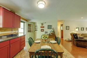 A dining area with a wooden table set for four, surrounded by chairs. A kitchen with red cabinets is visible to the left. - Hot Tub & Fire Pit! Creekfront Bryson City Cabin (Bryson City)