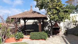 Un kiosque doté d’un toit de chaume, entouré d’un jardin agrémenté de plantes en pot et d’une table.