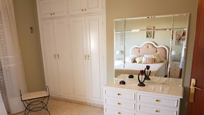 Une chambre dotée d’une grande armoire, d’une coiffeuse avec des tiroirs, d’un lit avec une tête de lit et d’un miroir qui reflète la pièce.