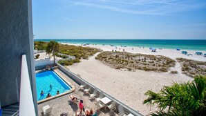 A poolside view with a beach and ocean in the background.