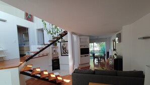 Un espacio habitable moderno con escaleras, suelo de madera, un sofá gris, zona de comedor y cocina.