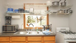 Uma cozinha com micro-ondas, fogão, pia e diversos utensílios em prateleiras.