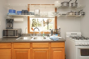 Una cocina con microondas, estufa, fregadero y diversos utensilios de cocina en estantes.