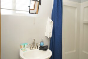 Un baño con lavamanos blanco, un espejo, cortina de ducha azul y artículos de aseo.