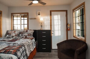 Un dormitorio con cama, cómoda, silla, ventilador de techo y ventana.
