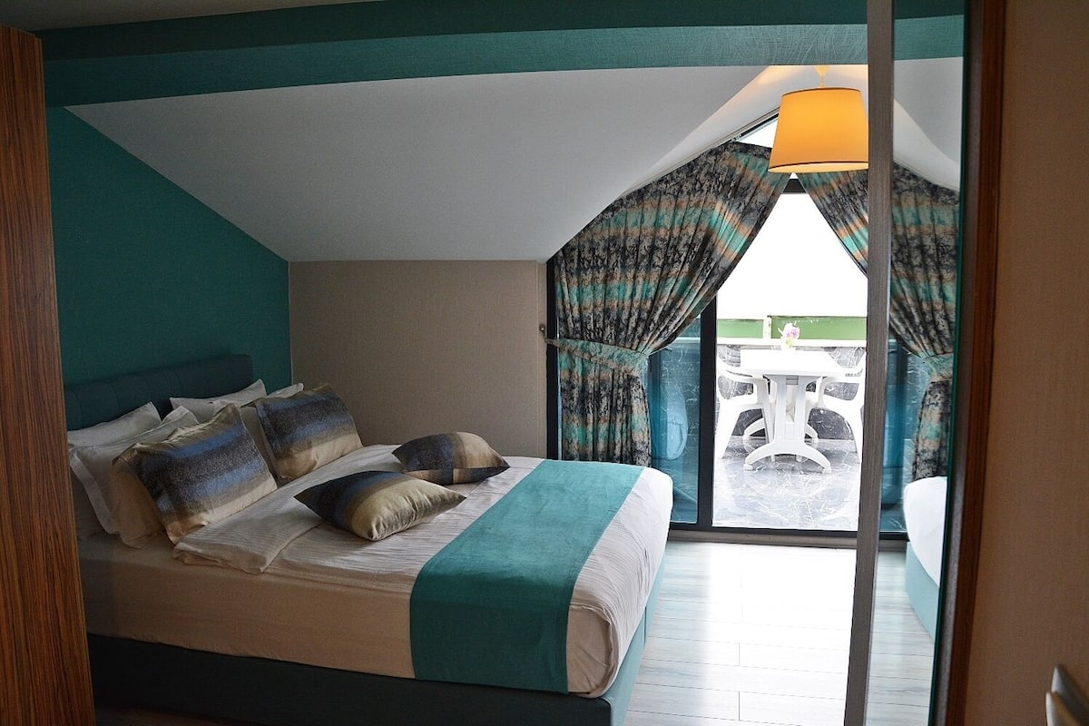 A bedroom with a bed, pillows, curtains, and a view of an outdoor patio.