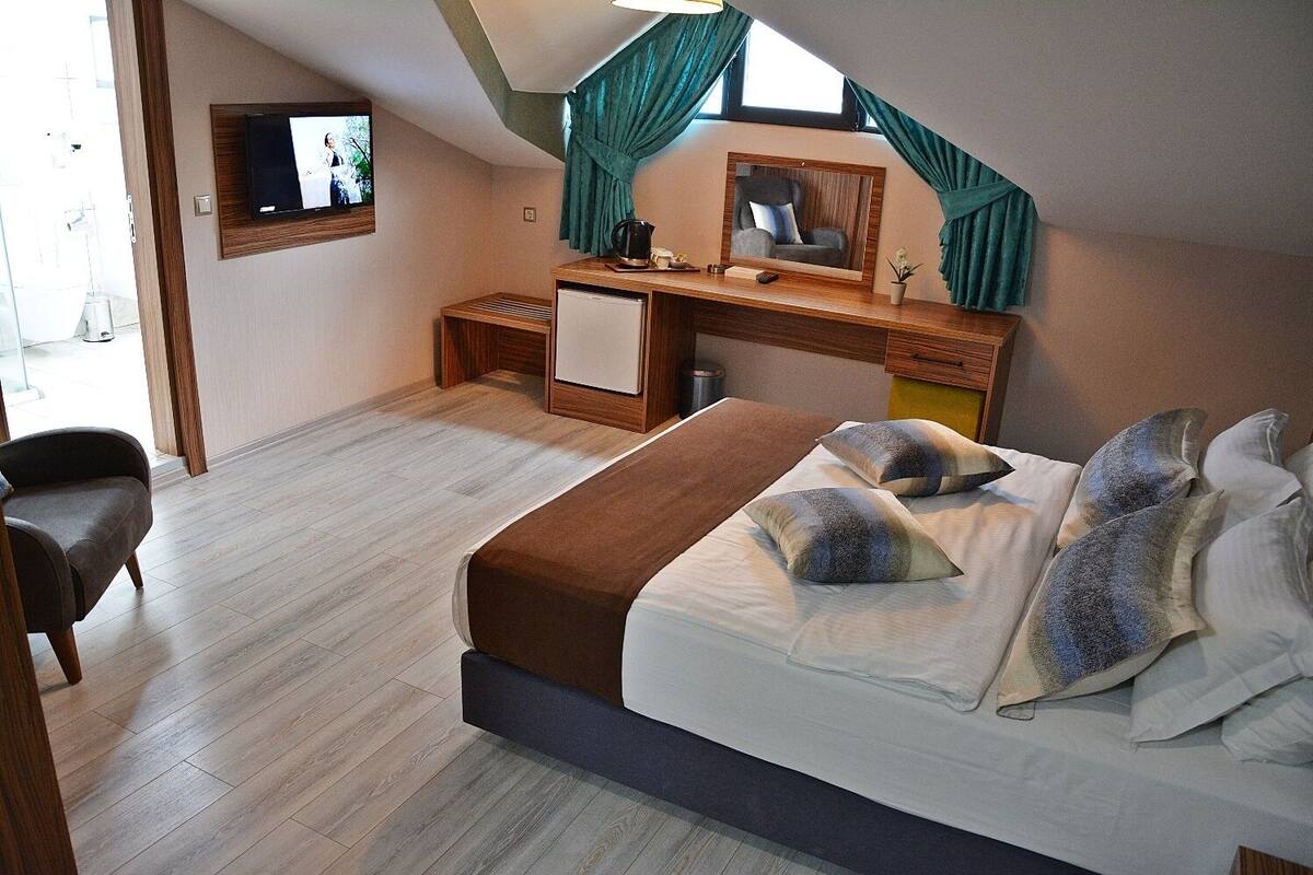 A bedroom with a bed, a desk, a chair, a TV, and a window with curtains.