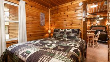 Une chambre confortable dans un chalet, avec un intérieur en bois, un lit recouvert d’une courtepointe à motifs, une petite table avec des chaises et un panneau accroché au mur.
