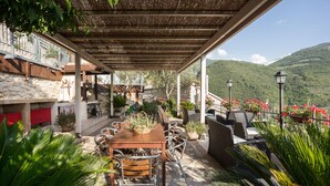 An outdoor patio with stone flooring, wooden tables, and chairs, surrounded by potted plants and overlooking a mountainous landscape. - LE ROCCHE - Under the Castle, SMERALDO Apartment with SPA and Black River View (Ferentillo)