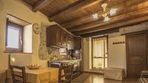 A rustic kitchen with wooden cabinets, a stone wall, and a dining area with a table and chairs. - LE ROCCHE - Under the Castle, SMERALDO Apartment with SPA and Black River View (Ferentillo)