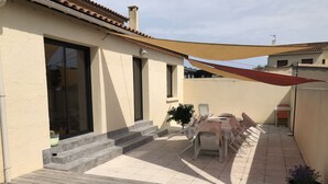 A patio with a table and chairs, a potted plant, and a wooden deck. - House with garden and pool near CAP D'AGDE (Agde)