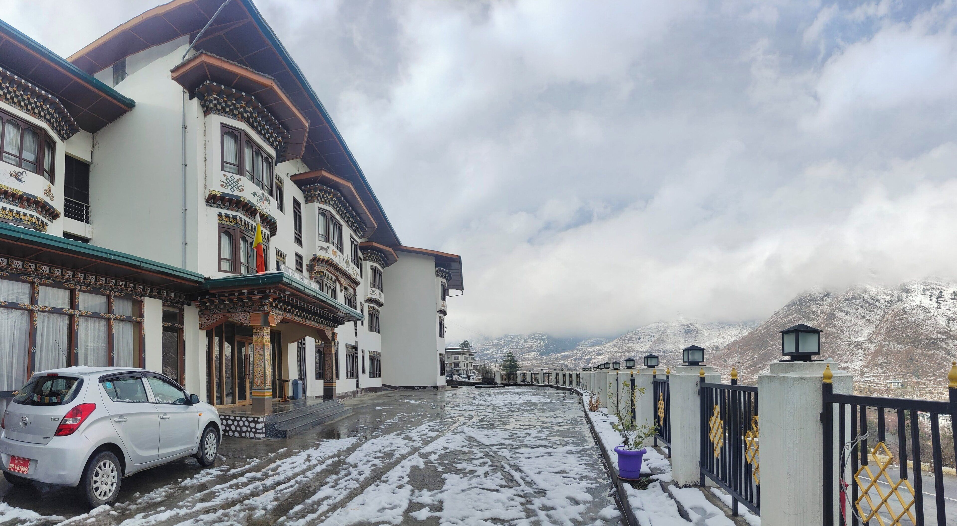A traditional building with a snow-covered ground, a parked car, and a mountainous backdrop.