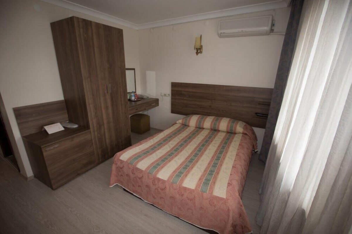 Un dormitorio con un armario de madera, una mesita de noche, una cama con ropa de cama a rayas y un aire acondicionado de pared.