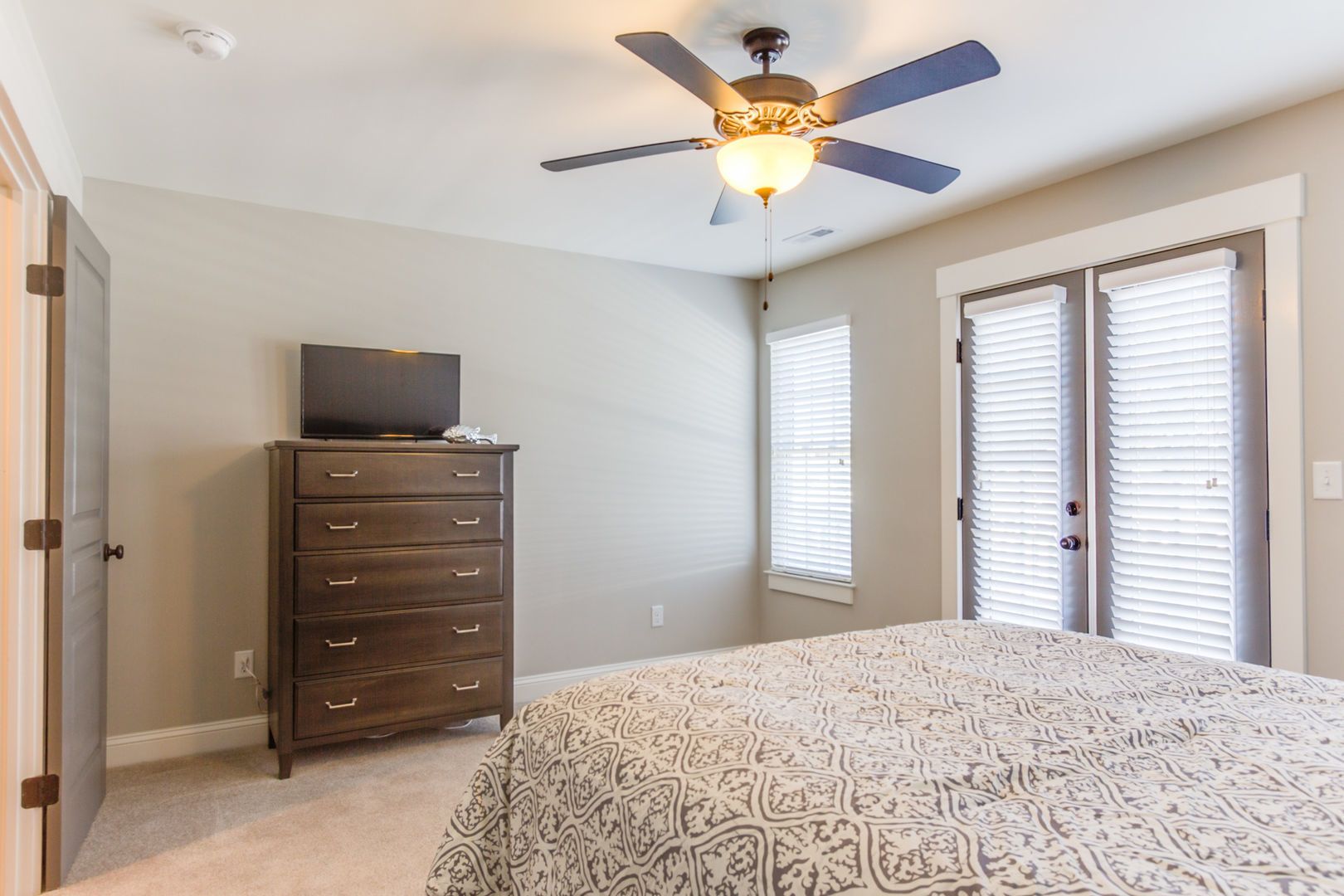 A bedroom with a bed, dresser, ceiling fan, and two windows with blinds.