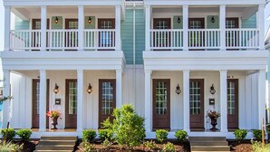 A symmetrical two-story house with a front porch, white exterior, and a small garden area.