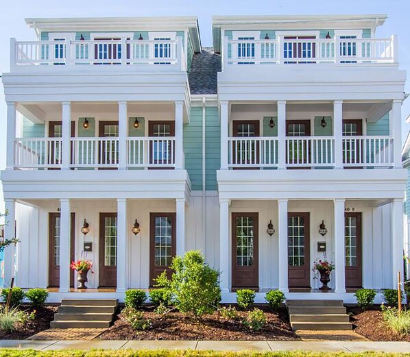A symmetrical two-story house with a front porch, white exterior, and a small garden area.