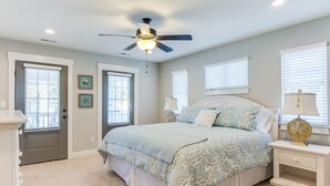A bedroom with a bed, a ceiling fan, a nightstand, and a door.