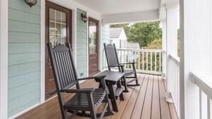 A porch with two wooden chairs and a table, light green siding, and a white railing.