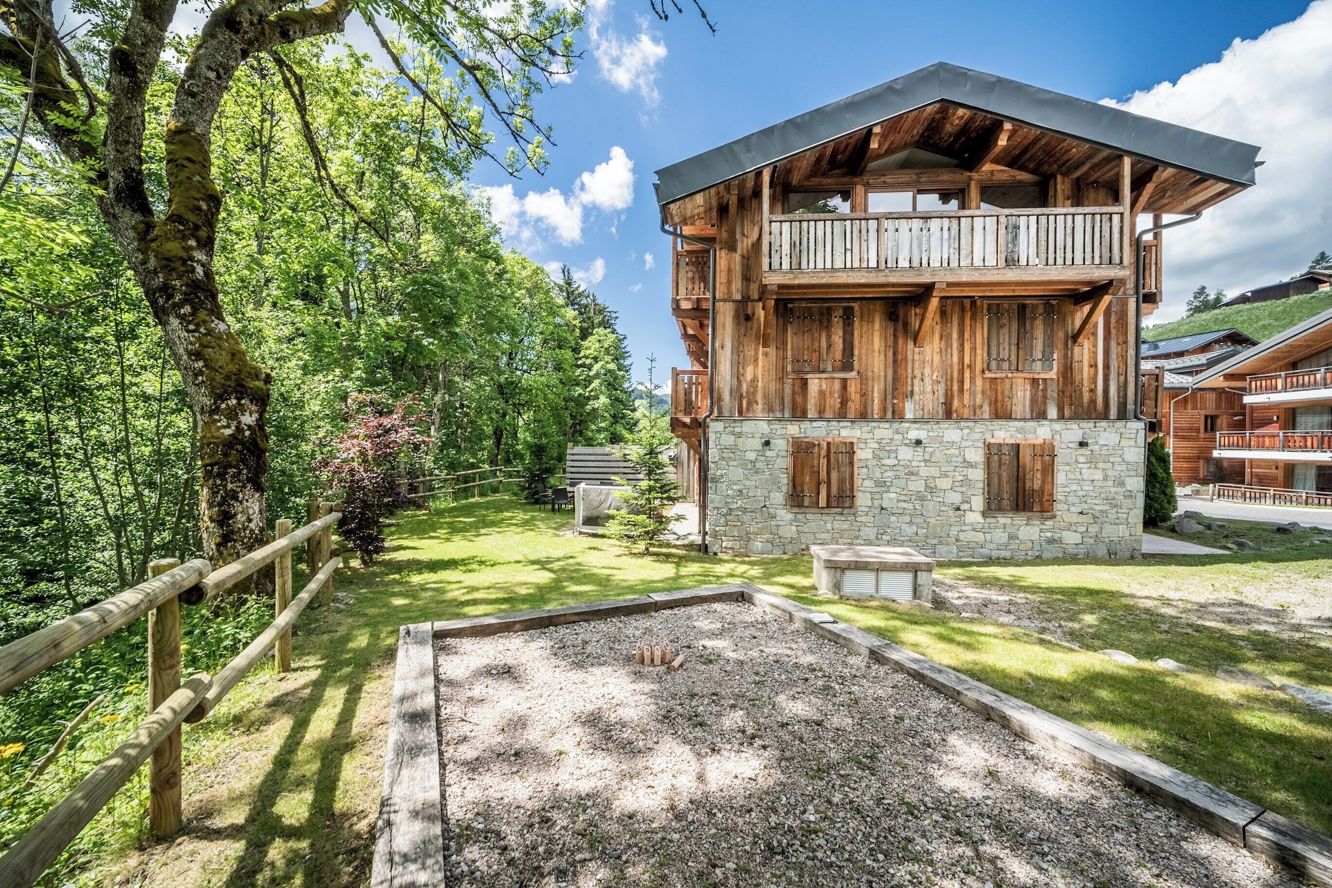 A wooden chalet with a stone base, a balcony, and a surrounding forested area.