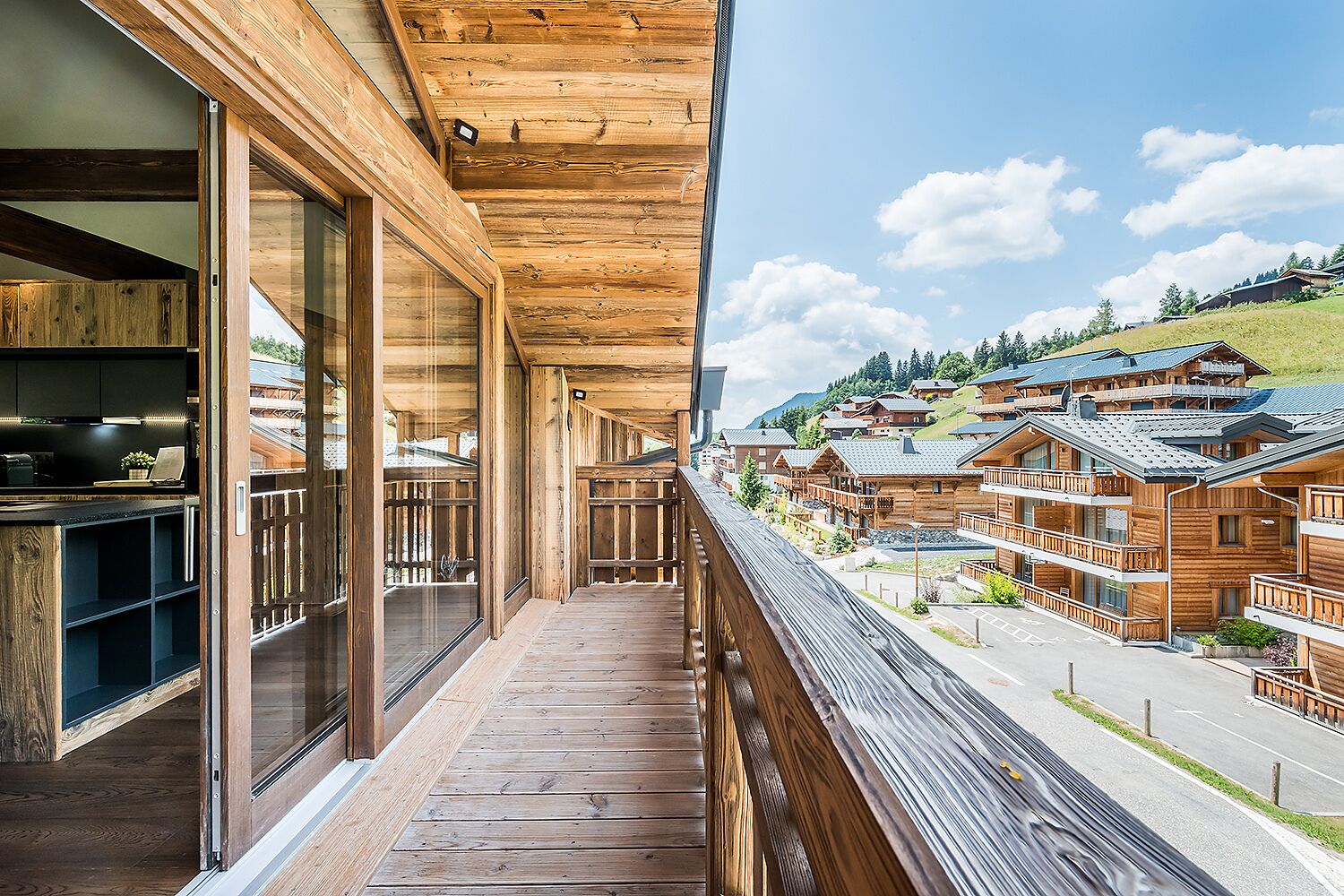 A wooden balcony with large windows overlooking a village with chalet-style buildings.