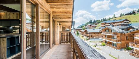 A wooden balcony with large windows overlooking a village with chalet-style buildings.