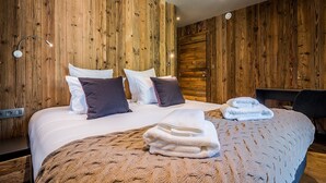 Ett hotellrum med en väggbeklädnad i trä, en säng med vita sängkläder och flera kuddar, ett sängbord med en lampa och en stol.