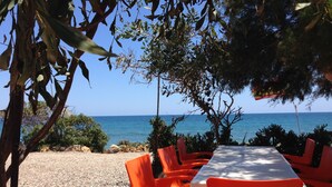 Ein Essbereich im Freien mit einem Tisch und orangefarbenen Stühlen, mit Blick auf einen Strand und das Meer im Hintergrund.