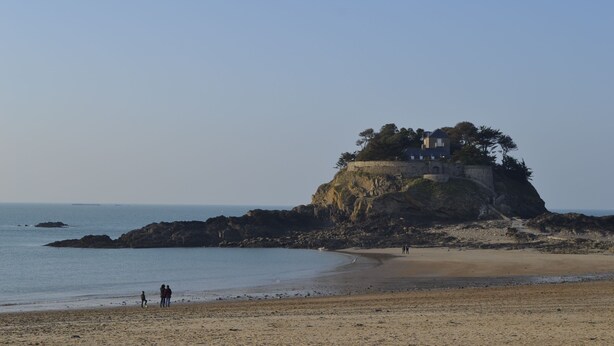 Ein Strand mit einem Felsen und einem Gebäude darauf.