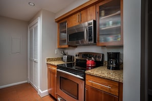 Compact kitchen with stainless steel microwave, toaster, and kettle, plus glass-fronted cabinetry and a white door with a louvered window.
