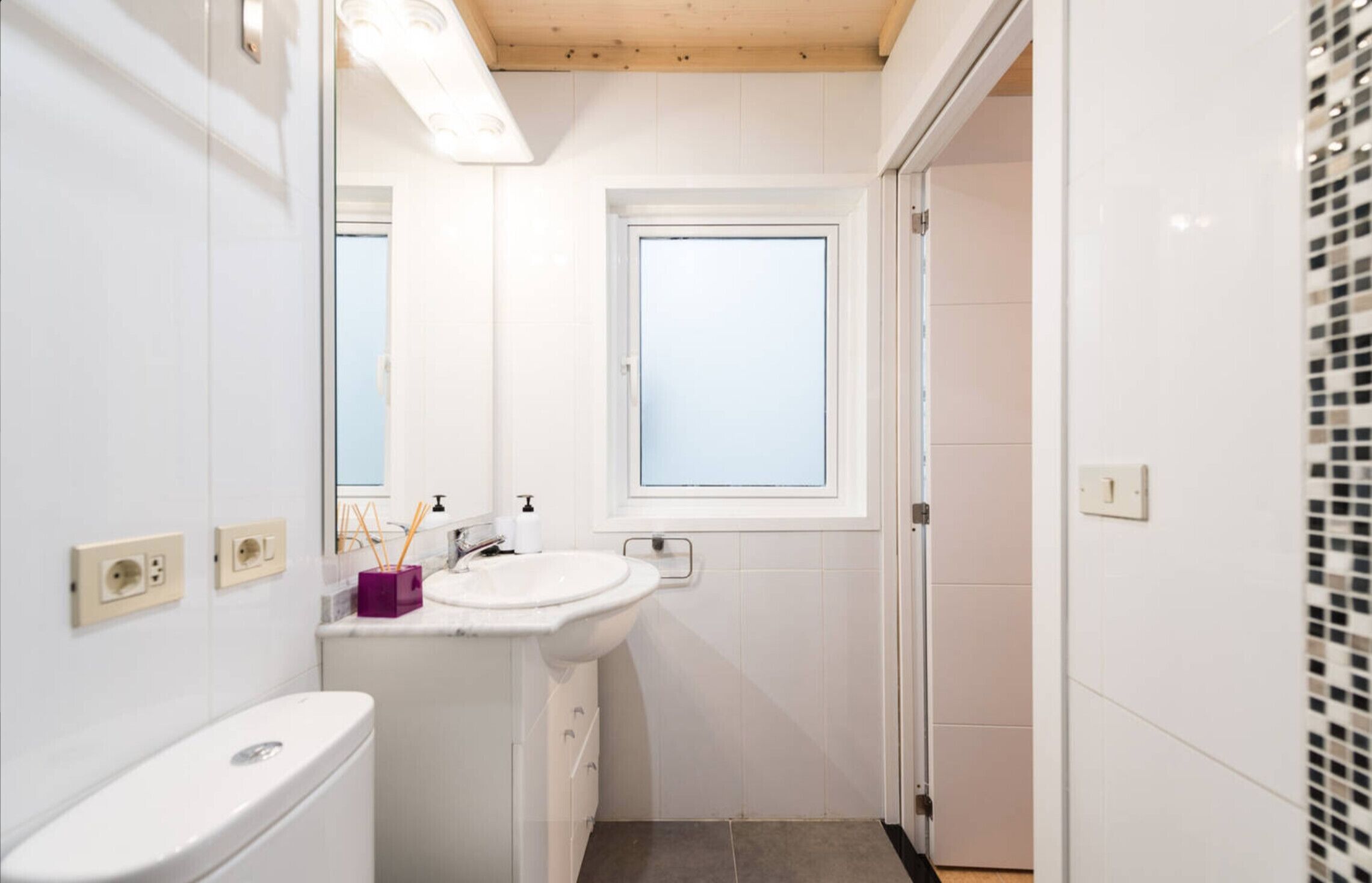 Un baño pequeño con un lavamanos blanco, un espejo, una ventana y un inodoro.
