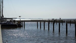 Eine Steg, der sich in ruhiges Wasser erstreckt, mit Booten am Ende vertäut.