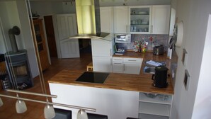 Eine moderne Küche mit weißen Schränken, einer Holzausziehtafel und einem eingebauten Backofen. Es gibt eine Essecke mit schwarzen Stühlen und einem Tisch.
