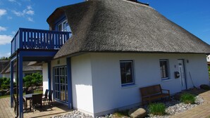Ein Haus mit Strohdach, einem Balkon, einer hölzernen Bank und einem kleinen Garten.